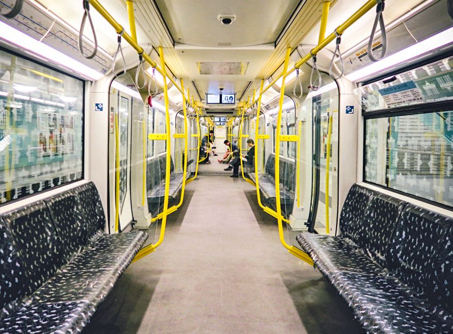 An underground station platform with a curved, tiled ceiling illuminated by bright overhead lighting. The platform features black tiled flooring with a textured yellow safety line along the edge. Ther