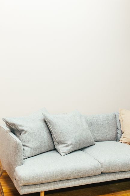 A mustard yellow armchair with a padded backrest and armrests, set against a plain white wall in a room with a concrete floor. The chair has a smooth, velvety fabric surface with visible buttons on th